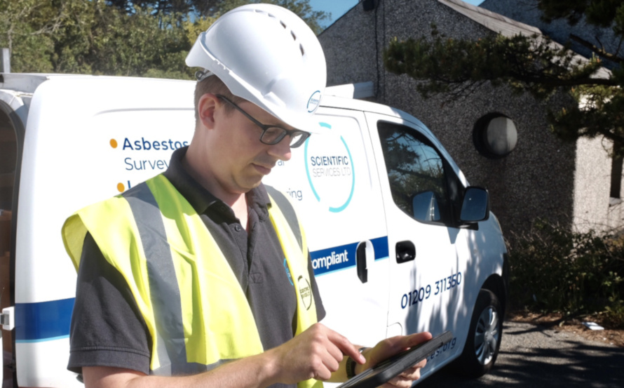 Surveyor looking at a tablet by a van after completing an asbestos survey