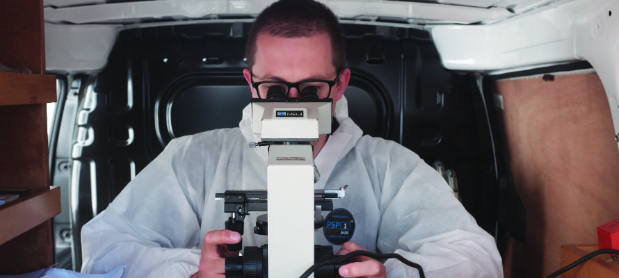 Asbestos analyst looking into a microscope within a mobile asbestos testing laboratory.